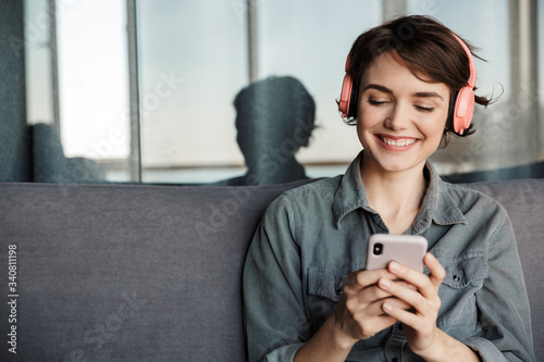 Image of nice young smiling woman using smartphone and headphones