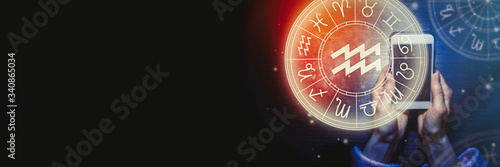 Female hands are holding a phone and an astrological circle with the zodiac sign Aquarius against the starry sky. Mobile Application for the horoscope. Banner. Copy space