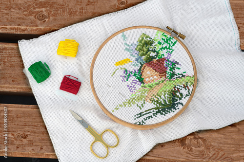 The round hoop with cross-stitch and embroidery accessories are on the wooden bench in outdoors.