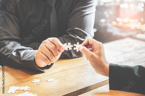 Businesspeople holding white jigsaw puzzle and connect together