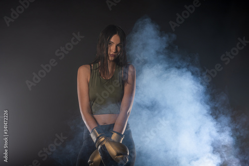 Closeup portrait of a female boxer posing with boxing gloves and looking at the camera with a smokey background