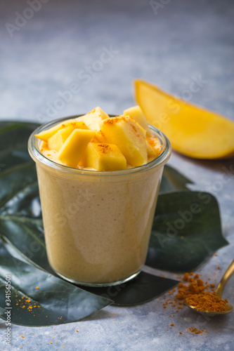 Yellow mango yogurt or smoothie on grey background. Turmeric Lassie or lassi in glass.
