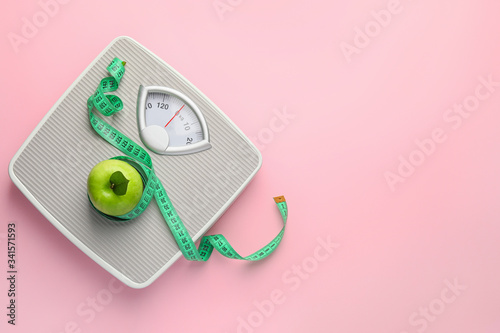 Weight scales with measuring tape and apple on color background. Slimming concept