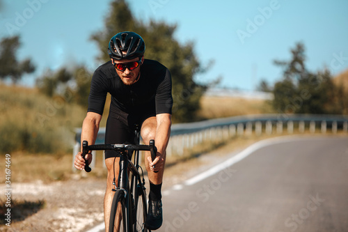 Front view of professional cyclist in sport outfit practising in cycling with blur background of green nature. Concept of summer activity and healthy lifestyle