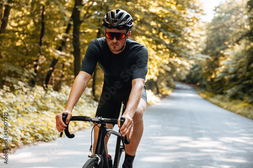 Bearded man with athletic body shape wearing sport clothing and mirrored glasses, riding bicycle among green forest. Concept of active and healthy lifestyle