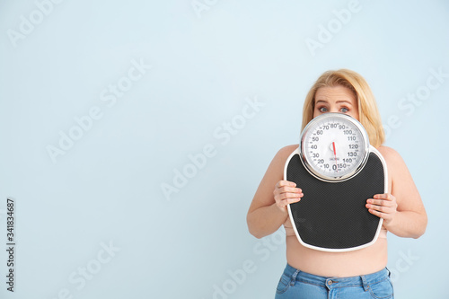 Troubled overweight woman with scales on color background. Weight loss concept