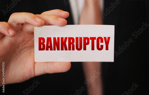 Bankruptcy on a card. Businessman holding a card with word Bankruptcy. Crisis business closing debts loss financial fiasko concept