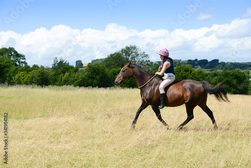 Pretty young woman riding bareback across the english countryside on her beautiful horse on a summers day.