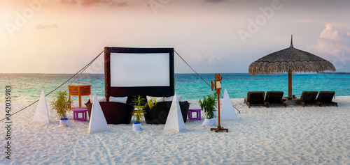 Eine privates Kino am Strand der Malediven bei Sonnenuntergang mit Kinoleinwand, gemütlichen Sitzkissen und luxuriöser Atmosphäre