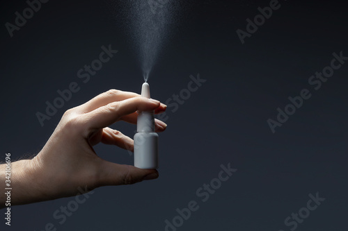 Man hand with a bottle of medication for runny nose during grippe on dark background. Treatment colds via a nasal spray.