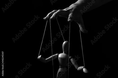 Conceptual image of a hand with strings to control a marionette in monochrome