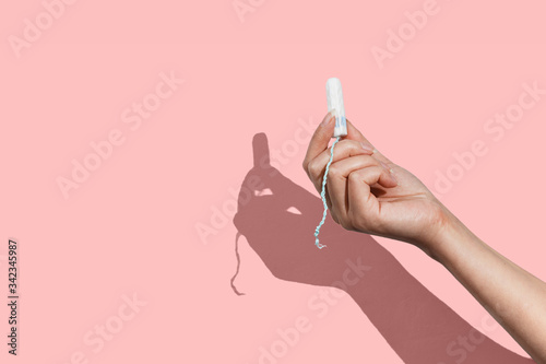 Woman's hand holding a clean cotton tampon on the pink background. Direct light.