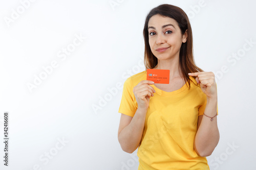 Giovane donna con i capelli lisci, indossa una T-Shirt gialla e tiene in mano una carta di credito arancione con grande entusiasmo , isolata su sfondo bianco