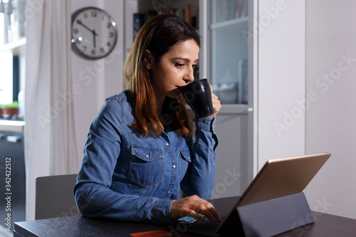 Ragazza chiara con i capelli lunghi utilizza la sua carta di credito per fare un ordine attraverso internet con il suo tablet, mentre sorseggia del tè da una tazza