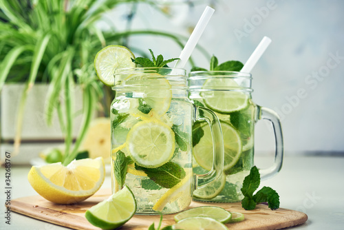Two glasses of homemade lemon, lime, and mint lemonade sit on the wooden dining table. Cold, refreshing summer lemonade or mojito.