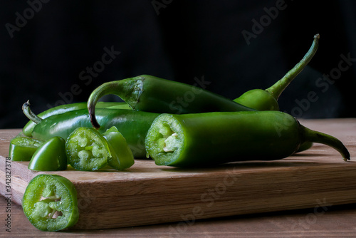 Chile serrano or serrano chilis on a wooden cutting board in a black background, ingredients for Mexican food cuisine. dark food or low key light photography, 