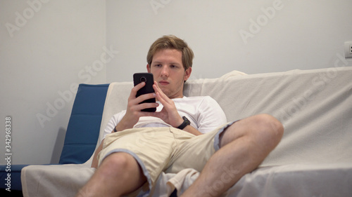 Casual Young Guy Sitting on Couch and Staring at Phone - Social Media and Smartphone Addiction