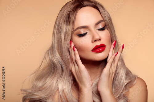 Makeup, manicured nails. Beauty portrait of blonde woman with red lips, long healthy shiny blond hair style. Sensual girl with bright makeup isolated on beige backhround.