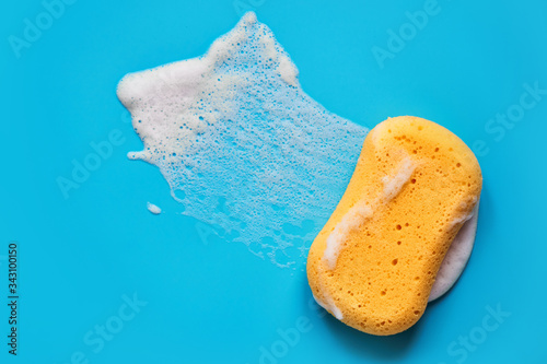 Yellow washing sponge in soap foam on a blue background isolated