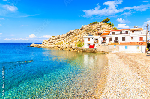 Snorkeler swimming in crystal clear azure sea water in Kokkari village with typical white houses on shore, Samos island, Aegean Sea, Greece
