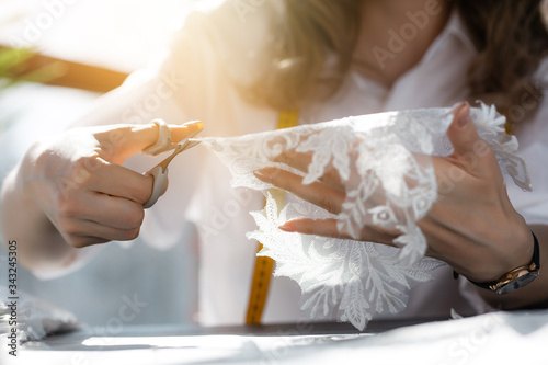Seamstress holding a part of wedding dresses lace and cuts off in the sun in the Studio