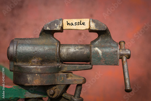 Vice grip tool squeezing a plank with the word hassle