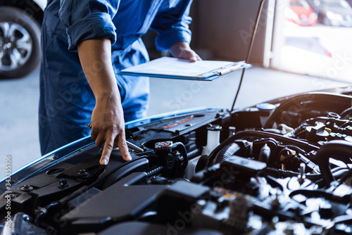 Car mechanic holding clipboard and checking to maintenance vehicle by customer claim order in auto repair shop garage. Engine repair service. People occupation and business job. Automobile technician