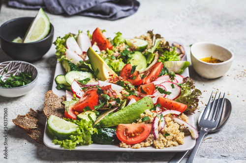 Quinoa salad with tomato, cucumber, radish and avocado on gray plate. Healthy vegan food concept.
