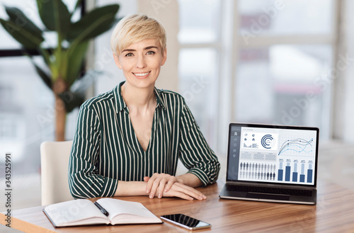 Smiling female manager sitting at desk with laptop
