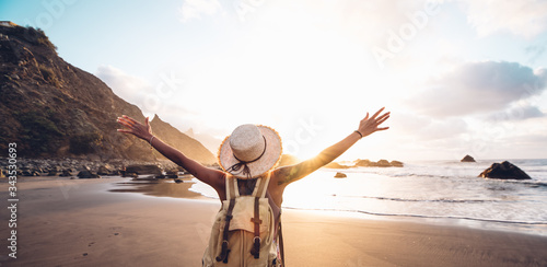 Happy woman with arms up enjoy freedom at the beach at sunset. Wellness, success, freedom and travel concept