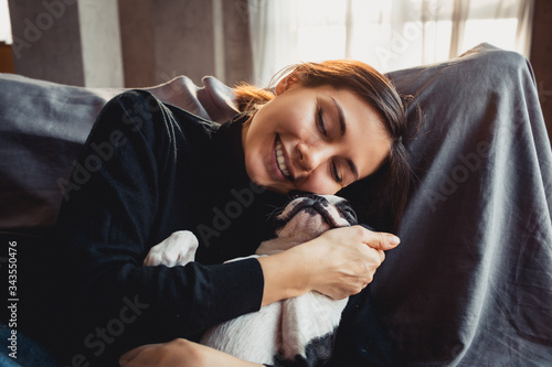 Young beautiful smiling woman hugging her pet - dog at home. Close up portrait.Beautiful young woman sitting on a sofa laughing and cuddling a dog.