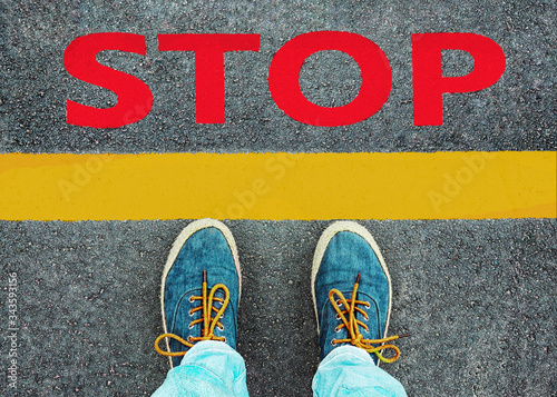 Women's feet in sneakers stand at the line with the inscription "stop".