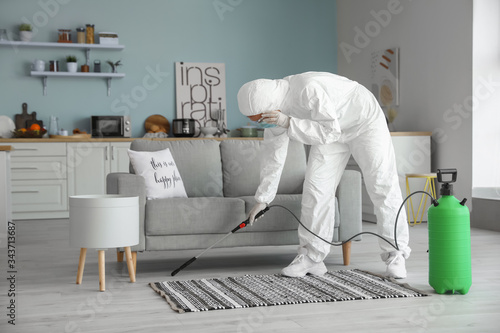 Worker in biohazard suit disinfecting house