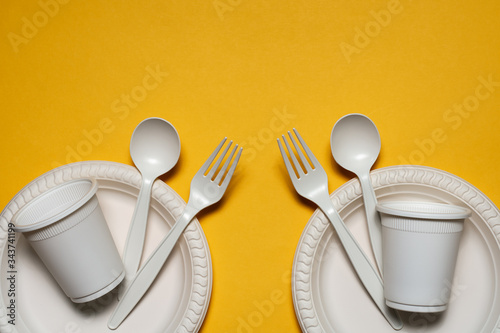 two sets of disposable spoons, forks, plates and glasses of corn starch on a yellow background. biodegradable tableware. environmentally friendly isolate. plastic replacement. modern biomaterials
