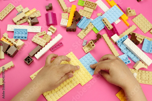 Hands of a child playing with colored blocks, bricks on a pink background