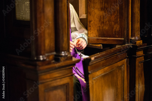 priest in the confessional recites the rosary awaiting penitent