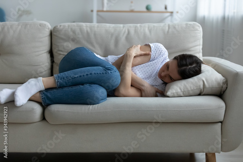 Depressed young woman lying on couch on living room feeling distressed lonely after breakup or divorce, upset unhappy millennial female mourn yearn on sofa, suffer after miscarriage or abortion