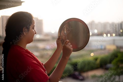 Young indian girl making noise with a plate and spoon as a mark of respect for essential healthcare workers, medical personel, doctors, policemen and more during the coronavirus lockdown in India
