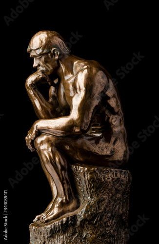 A bronze replica statue of Rodin's Thinker on a black marble background