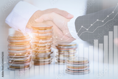 Successful cooperative, teamwork, and joint venture concept; double exposure of handshake and coins stack, with growing trend graph.