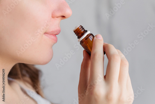 Aromatherapy: a girl with beautiful skin holds a bottle of essential oil near her nose and inhales. Close up, bright marble background.