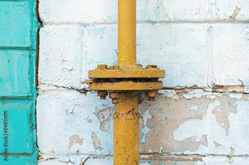 An old yellow gas pipe with flange connection. A white brick on peeling wall. Abstract background