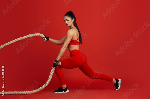 Training active. Beautiful young female athlete practicing in studio, monochrome red portrait. Sportive fit brunette model with ropes. Body building, healthy lifestyle, beauty and action concept.