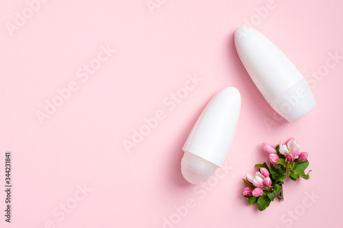 Blank roll-on deodorant bottles with blossom flowers on pink background. Natural organic antiperspirant, female sweat protection product concept. Flat lay, top view
