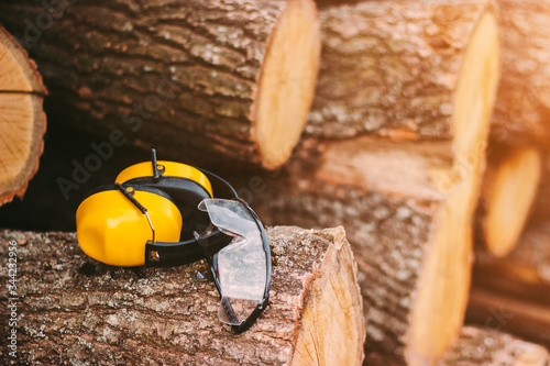 Conceptual image of protective glasses and headphones on fresh cut pine tree logs at sawmill. Professional workwear for personal protection at wood production factory. Earmuffs and protective eyewear