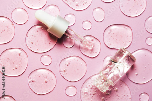 Liquid gel or serum drops with pipette on pink background in macro. Flat lay style.