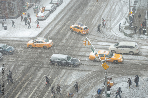 high angle view of winter new york city intersection with taxi cabs, cars, suvs, and people walking on a snowy white snow covered streets and walkways