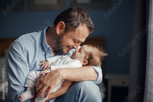 Middle age Caucasian father kissing sleeping newborn baby girl. Parent holding rocking child daughter son in hands. Authentic lifestyle parenting fatherhood moments. Single dad family home life.