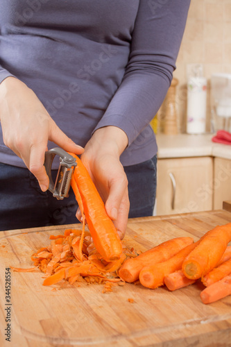 Kobiece dłonie obierają marchew za pomocą obieraczki do warzyw.