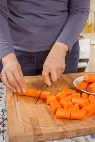 Marchewka krojona przez kobietę w kuchni za pomocą noża kuchennego.